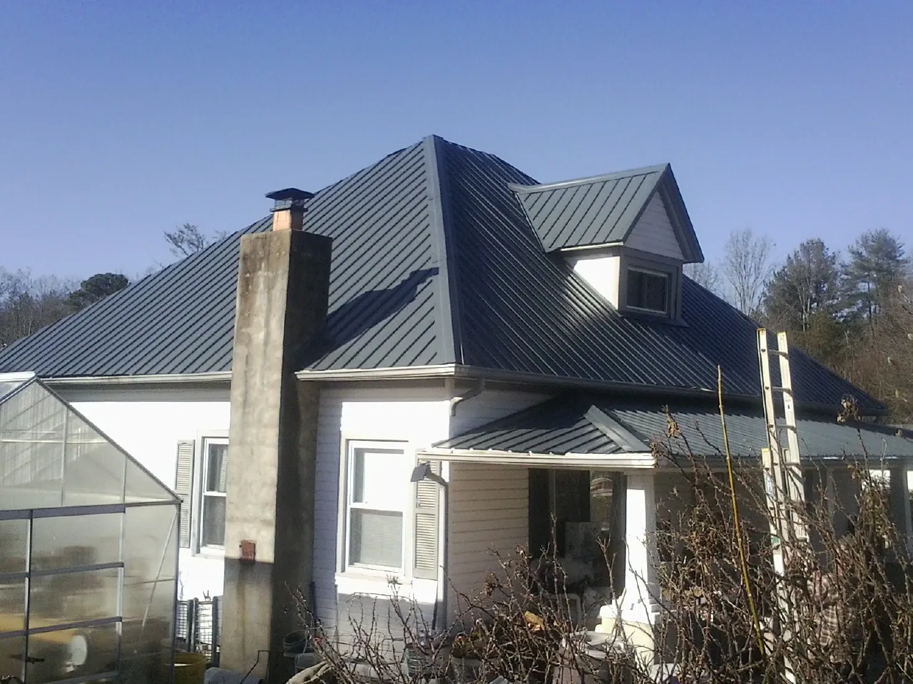 Dark blue standing seam metal roof on a white farmhouse with dormer — Slate & Tile Roof Repair by Roofing Brothers in Orgas