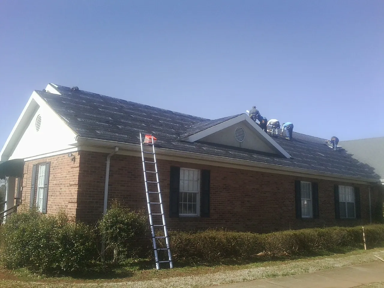 Crew tearing shingles off a brick ranch roof with a ladder set — Metal Roof Repair work by our crew in Orgas