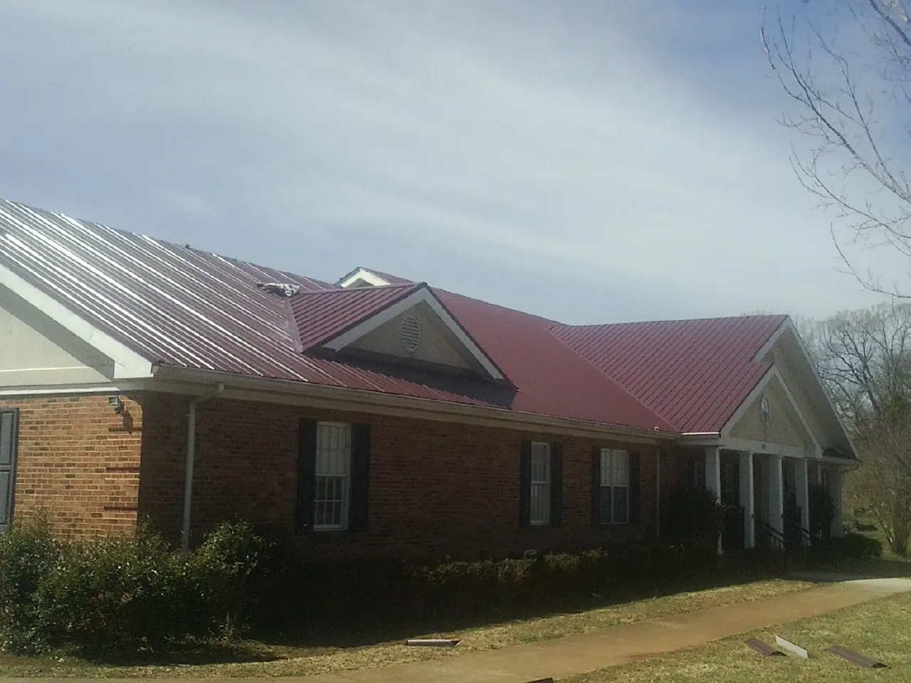 Red metal roof with gabled entries on a long brick building, from a Hail Damage Roof Repair job in Orgas
