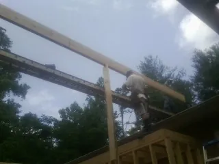 Carpenter setting a ridge beam over a new addition frame in Orgas