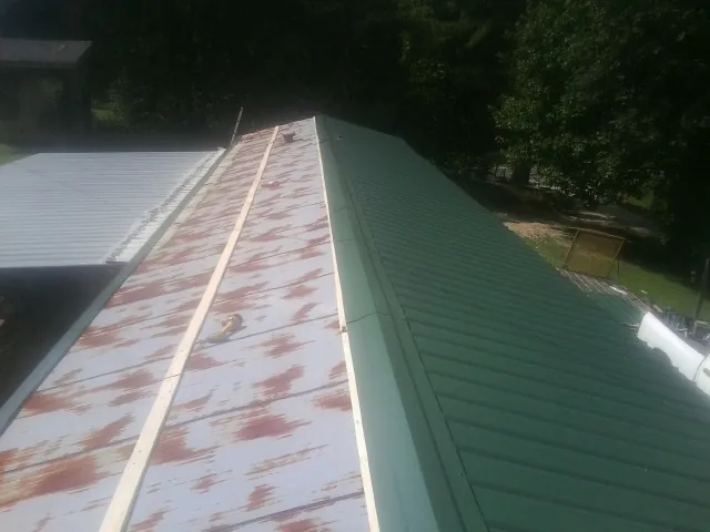 Old rusted panels beside newly installed green metal roofing — Wind Damage Roof Repair by Roofing Brothers in Orgas