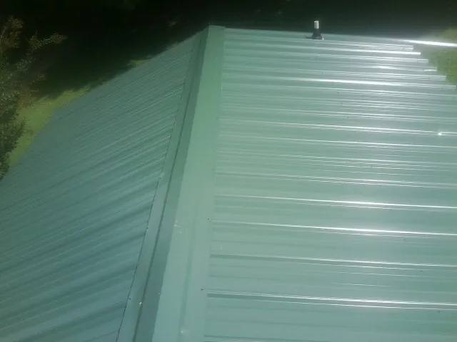 New green metal panels meeting at the ridge of a roof — Flat Roof Repair work by our crew in Orgas
