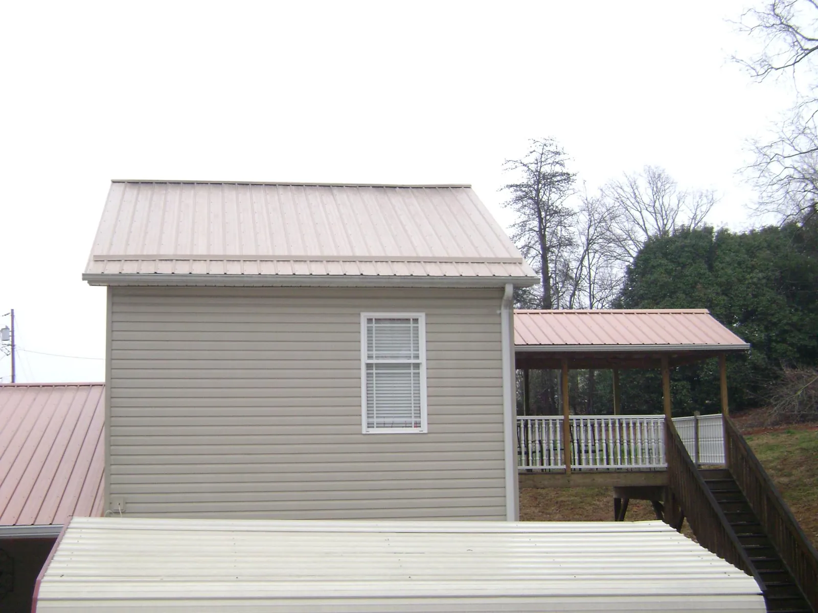 Tan metal roofs on a two story addition and attached porch, from a Roof Replacement job in Orgas